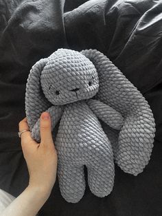 a hand holding a gray stuffed animal on top of a black bed cover with pillows