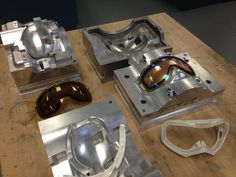 some metal parts sitting on top of a wooden table with goggles and other items