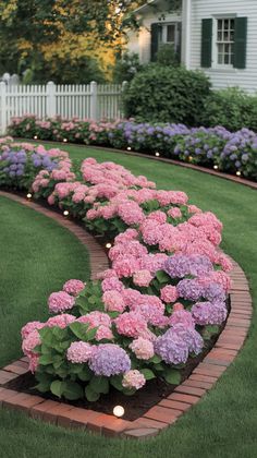 pink and purple flowers in a garden with brick edging on the side of it