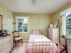 a bedroom with floral wallpaper and pink bedding, dressers, and mirror