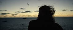 a woman looking out over the ocean at sunset