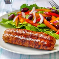 two sausages on a plate next to a salad