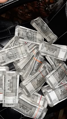 a pile of twenty dollar bills sitting on top of a black leather bag in someone's hand