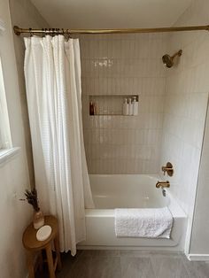 a bathroom with a white bathtub and shower curtain next to a wooden stool in front of the tub