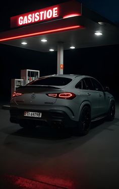 a car is parked in front of a gas station at night with its lights on