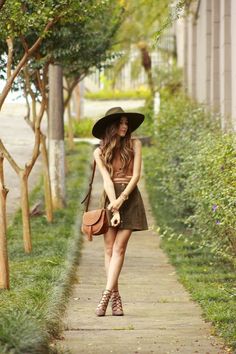a woman walking down a sidewalk wearing a hat and holding a handbag in her right hand