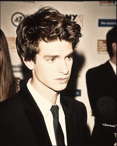 a young man in a suit and tie standing next to a microphone on the red carpet