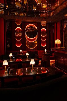 a dimly lit restaurant with red lighting and round chandeliers hanging from the ceiling