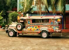 an old bus painted with colorful designs parked in front of a building and palm trees