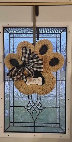 a teddy bear wreath hangs on the front door glass with a ribbon tied around it