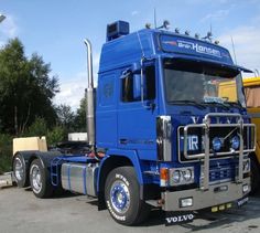 a large blue truck parked in a parking lot next to another yellow truck and some trees