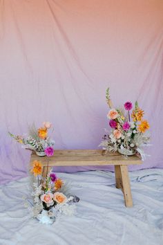 two wooden benches sitting on top of a bed covered in blankets next to vases filled with flowers