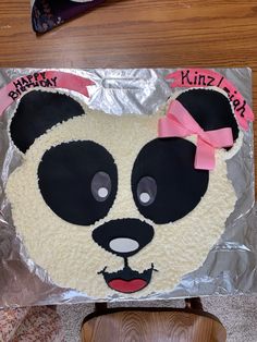 a panda bear cake with pink bows on it's head is sitting on a chair
