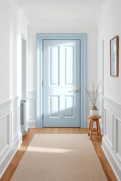 an empty hallway with a blue door and wooden stool in the center, along with white walls