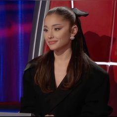 a woman with long hair sitting in front of a red and blue background wearing a black suit
