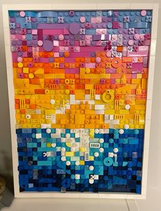 an art piece made out of legos on display in a white frame with a blue, yellow and red background