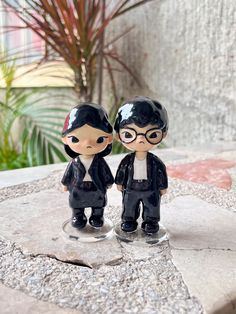 two small figurines sitting on top of a rock