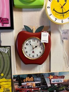 a red apple shaped clock sitting on top of a white wall next to other clocks