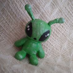 a green toy with black eyes sitting on top of a white cloth covered tablecloth