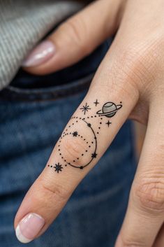 a woman's hand with a small star and planet tattoo on the middle finger