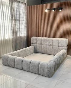 a large gray couch sitting in front of a wooden paneled wall with curtains on it
