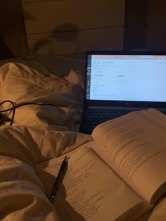 an open laptop computer sitting on top of a bed next to an open notebook and pen