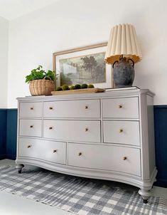 a white dresser sitting next to a blue wall with a painting on top of it