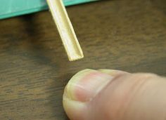 a finger is pointing at a matchstick on a table with a piece of paper in the background