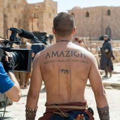 a man with tattoos on his back is being filmed by a cameraman in front of an ancient building