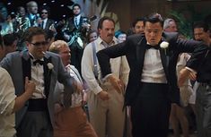 a man in a tuxedo is dancing with other men and one has his hand on his hip