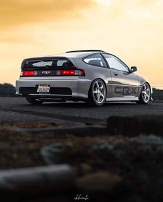 the back end of a silver car parked on top of a parking lot at sunset