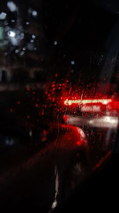 the rear view mirror of a car with rain on it's glass and red tail lights