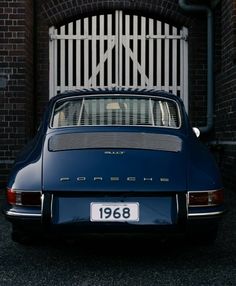 an old blue porsche parked in front of a brick building with a white iron gate