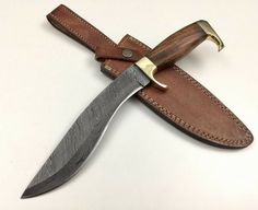 a knife that is sitting on top of a leather sheath with a gold handle and blade