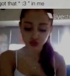 a woman with long hair wearing a white tank top and looking at her cell phone