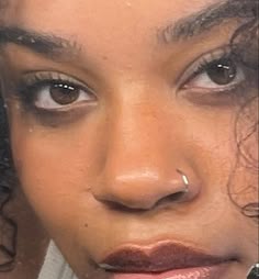 a close up of a person with dark hair and piercings on her nose looking at the camera