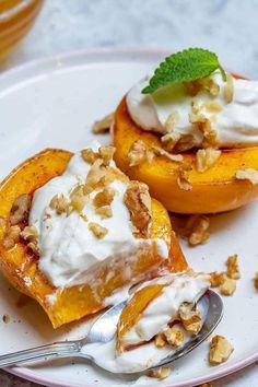 two pieces of peaches with whipped cream and walnuts on a plate next to a fork