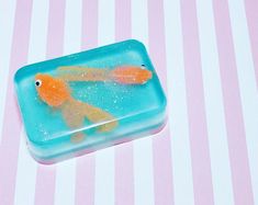 an orange and yellow fish in a blue container on a pink and white striped surface