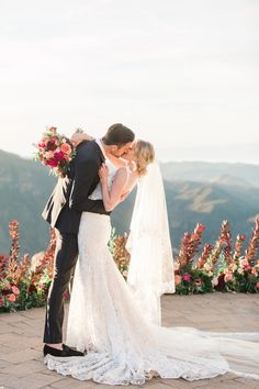 a bride and groom kissing on top of a mountain