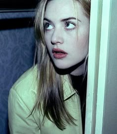 a woman with long blonde hair and blue eyes is looking at the camera while standing in front of a door