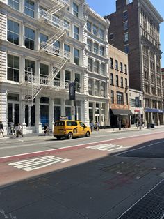 a yellow van parked in front of a tall white building on a city street with people walking by