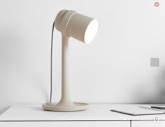 a desk lamp sitting on top of a white table next to a laptop and pen