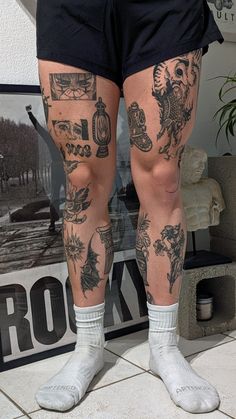 the legs and ankles of a person with tattoos on their body, standing in front of a poster
