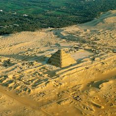 an aerial view of a pyramid in the middle of desert land with trees and fields behind it