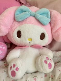a pink and white stuffed animal with a blue bow on it's head sitting on a bed