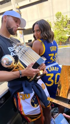 a man and woman standing next to each other in front of a car holding trophies