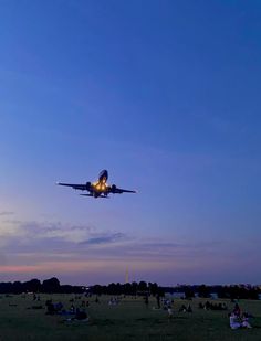 an airplane is flying low to the ground as people sit on the grass and watch