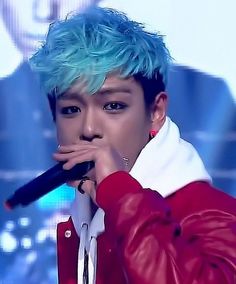 a man with blue hair is holding a microphone in his hand and wearing a red leather jacket
