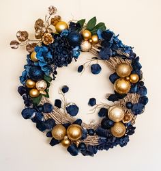a wreath with blue and gold ornaments hanging from it's side on a white wall