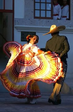 a man and woman in mexican dress dancing on the street at night with their arms around each other